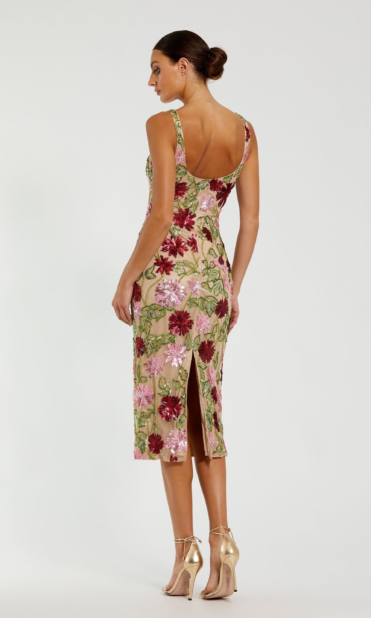 A woman stands in the Mac Duggal 6124 Beaded Midi Wedding Guest Dress, featuring a sleeveless fitted silhouette, nude base, pink/green/red floral beading, back slitโstyled elegantly with metallic high heels.